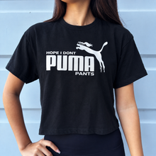 Load image into Gallery viewer, A woman wearing a black short-sleeve crop top T-shirt with a white graphic print that reads 'HOPE I DON'T PUMA PANTS' and features the Puma cat logo, posed against a light blue paneled wall.
